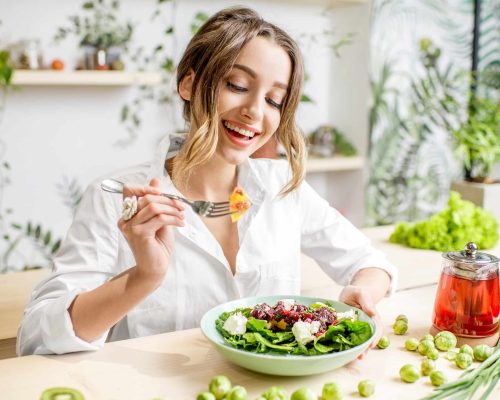 Young,Woman,Eating,Healthy,Food,Sitting,In,The,Beautiful,Interior Young woman eating healthy food sitting in the beautiful interior with green flowers on the background